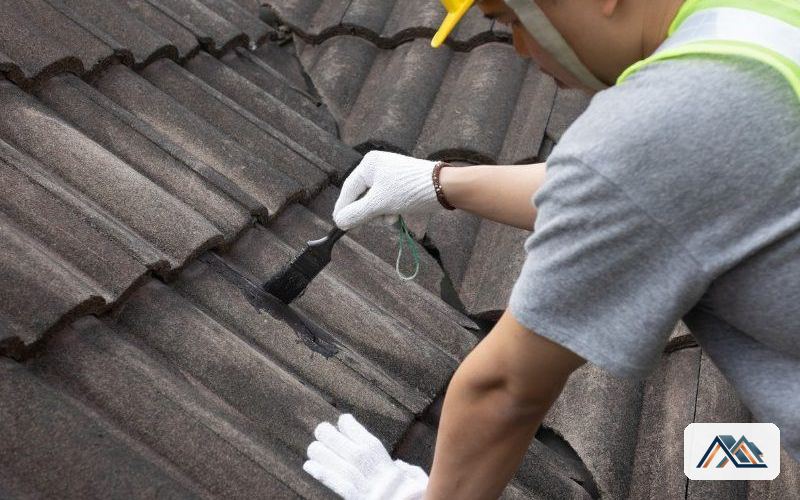 Técnico con guantes comprobando una pieza suelta de un tejado de teja oscura