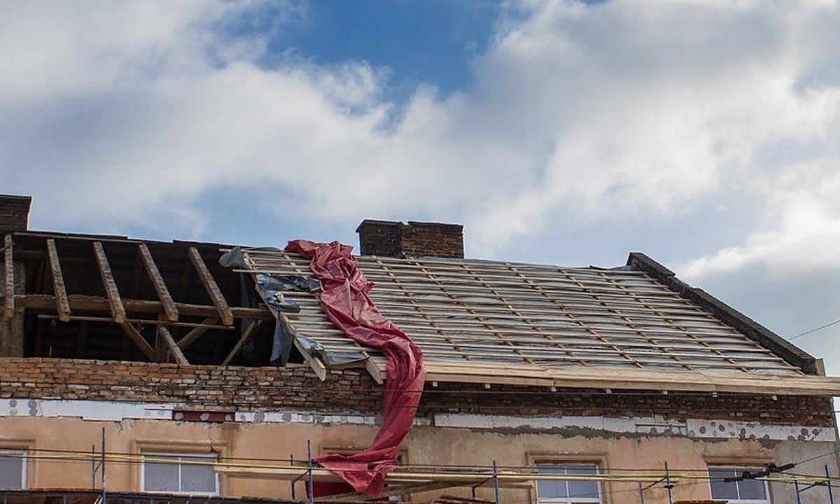 Tejado dañado por un temporal Cubierta de una vivienda sin teja en parte del faldón, con los rastreles a la vista y una lona roja colgando