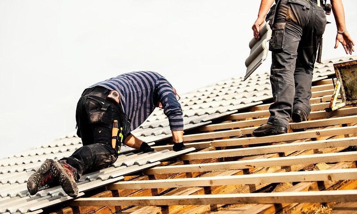 Operarios trabajando sobre el entramado de rastreles de madera de una cubierta abierta