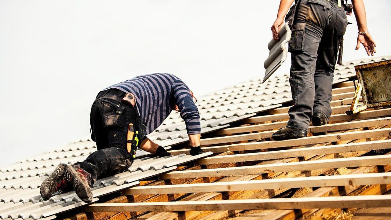 Equipo de tejadores colocando placas sobre la estructura de madera de una cubierta en Lugo