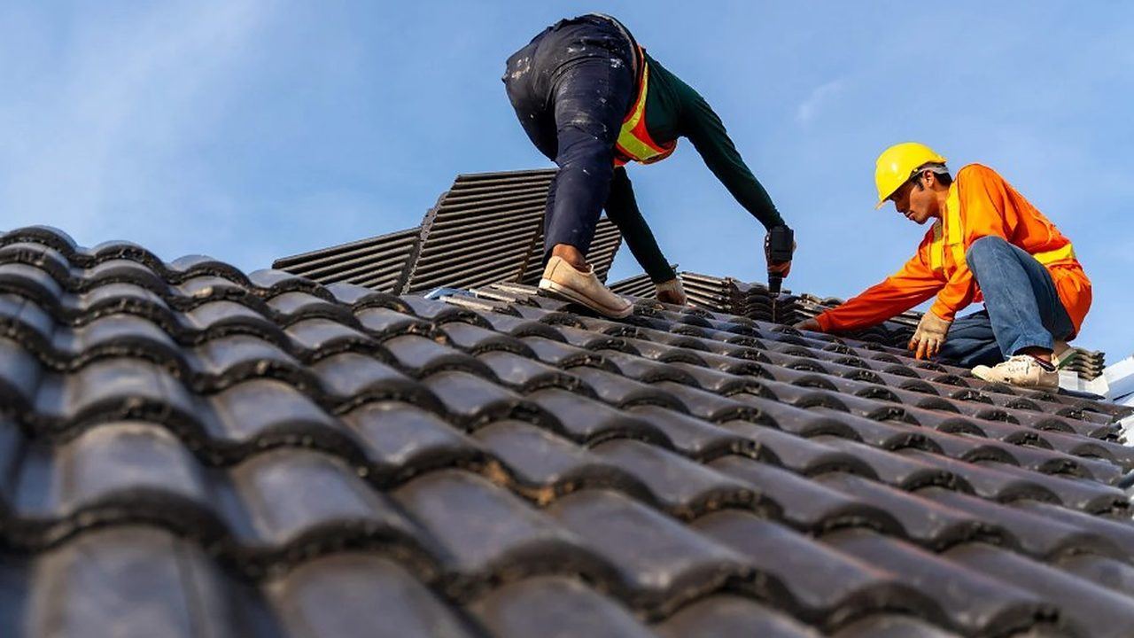 Reparación de tejados en Lugo Dos tejadores atornillando teja sobre la cubierta de una vivienda en Lugo