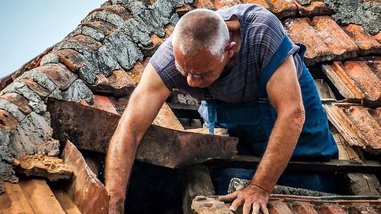 Tejador retirando teja partida durante el retejado de una vivienda de Lalín, Pontevedra